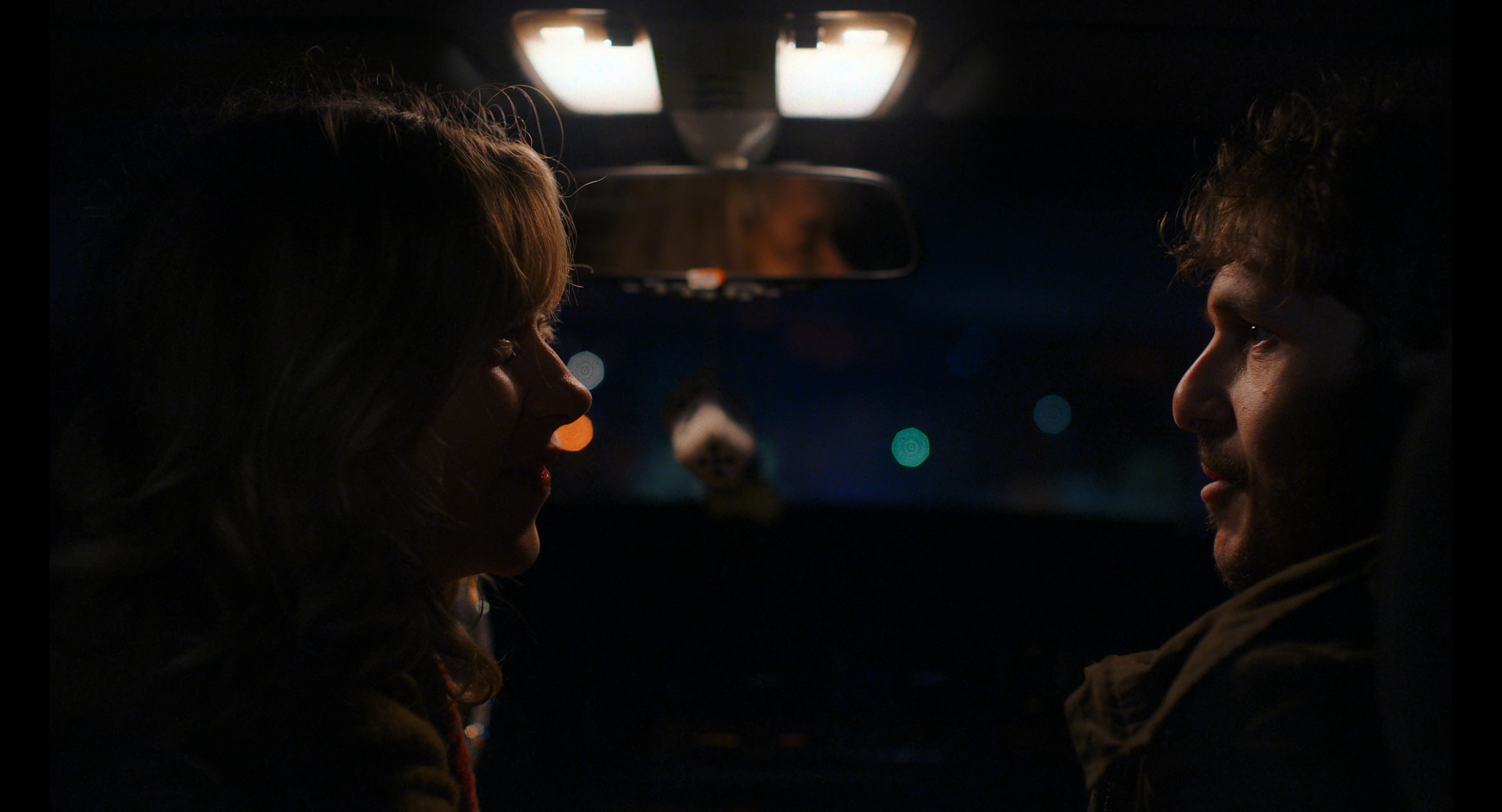 Dimly lit interior still with a character in quiet tension.